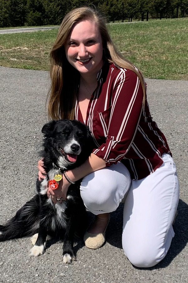 Dr. Runser-female wearing a maroon shirt and white pants kneeling down next to a black shepherd dog